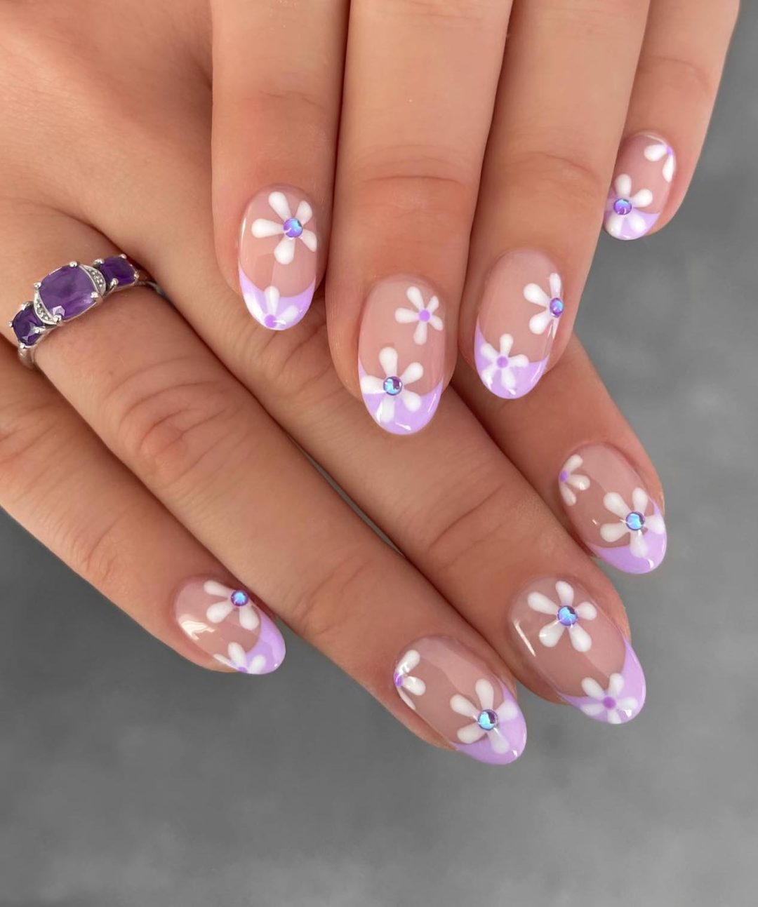 Light purple French tip nails with daisies and crystals.