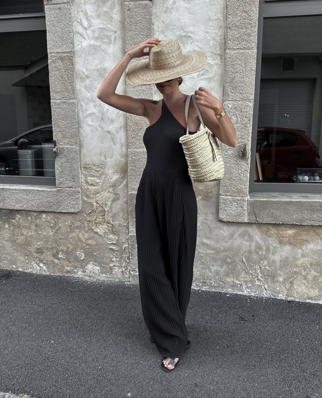 Girl wearing a black swimsuit with black plazzo pants and a straw hat and bag