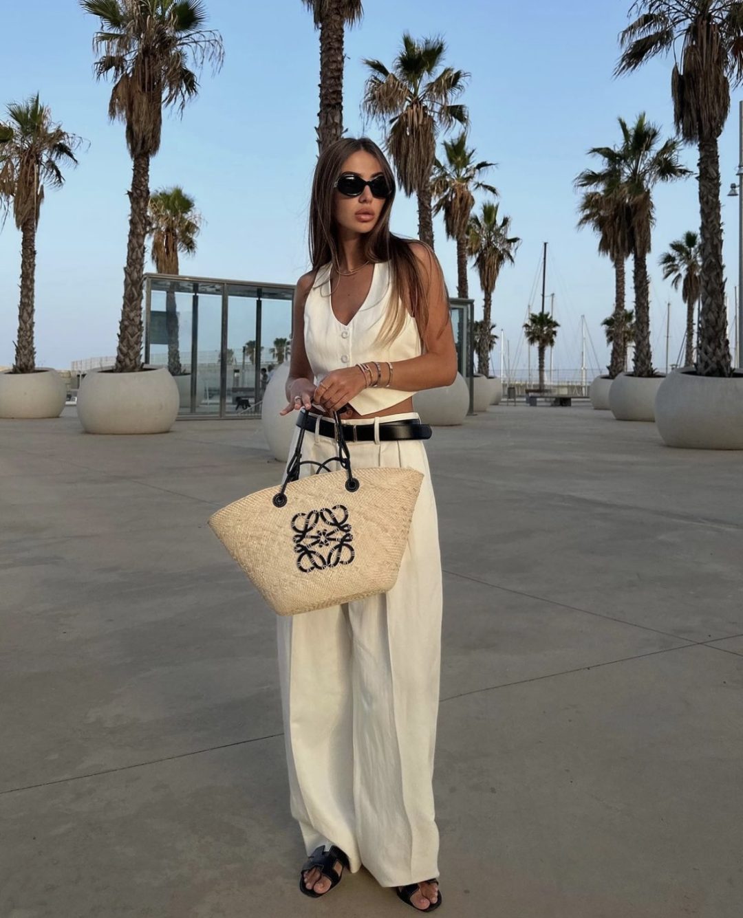 Girl wearing a white cropped waistcoat with white palazzo pants and a straw loewe bag