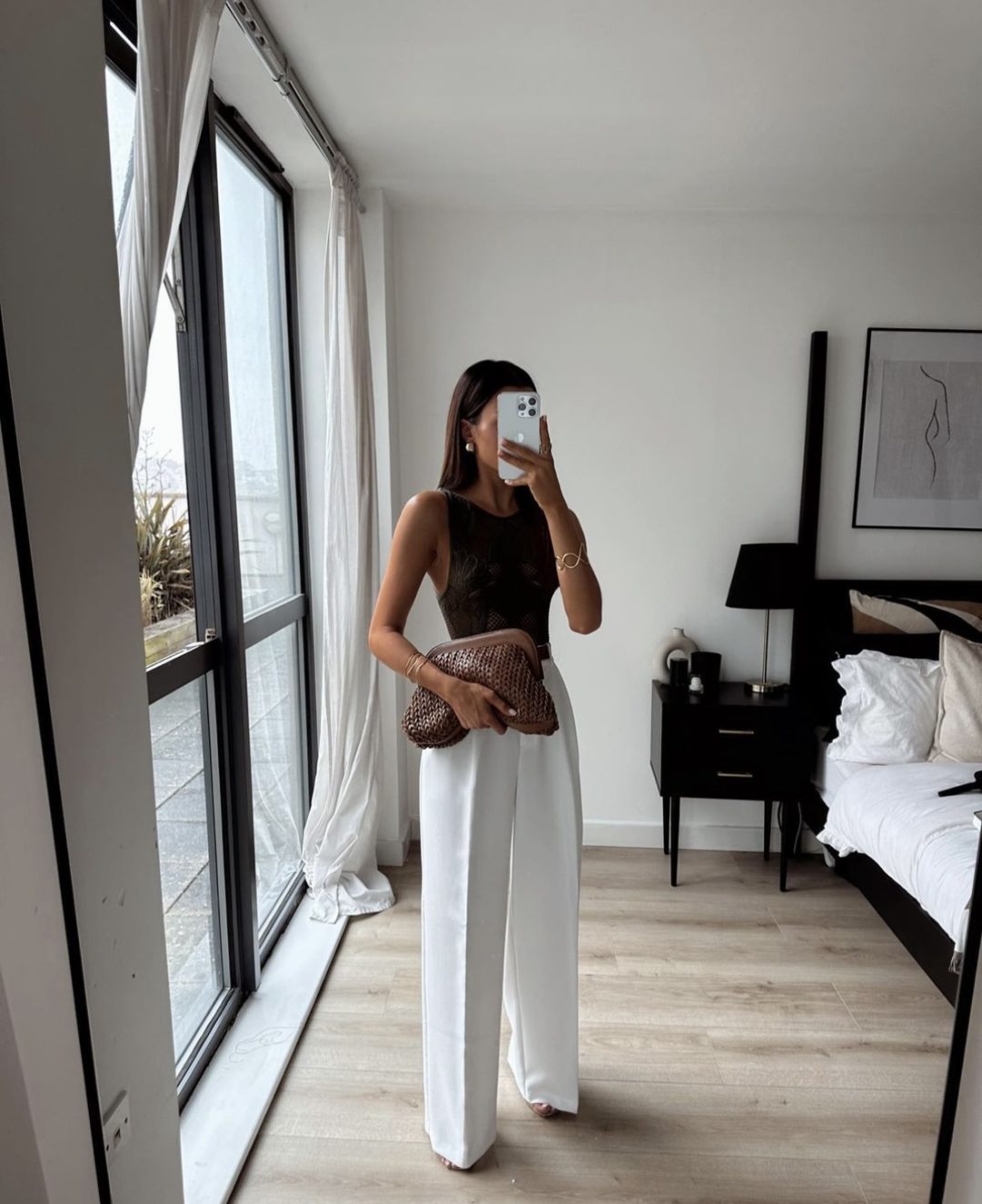 Girl wearing a black bodysuit with white wide leg palazzo pants and a brown raffia bag