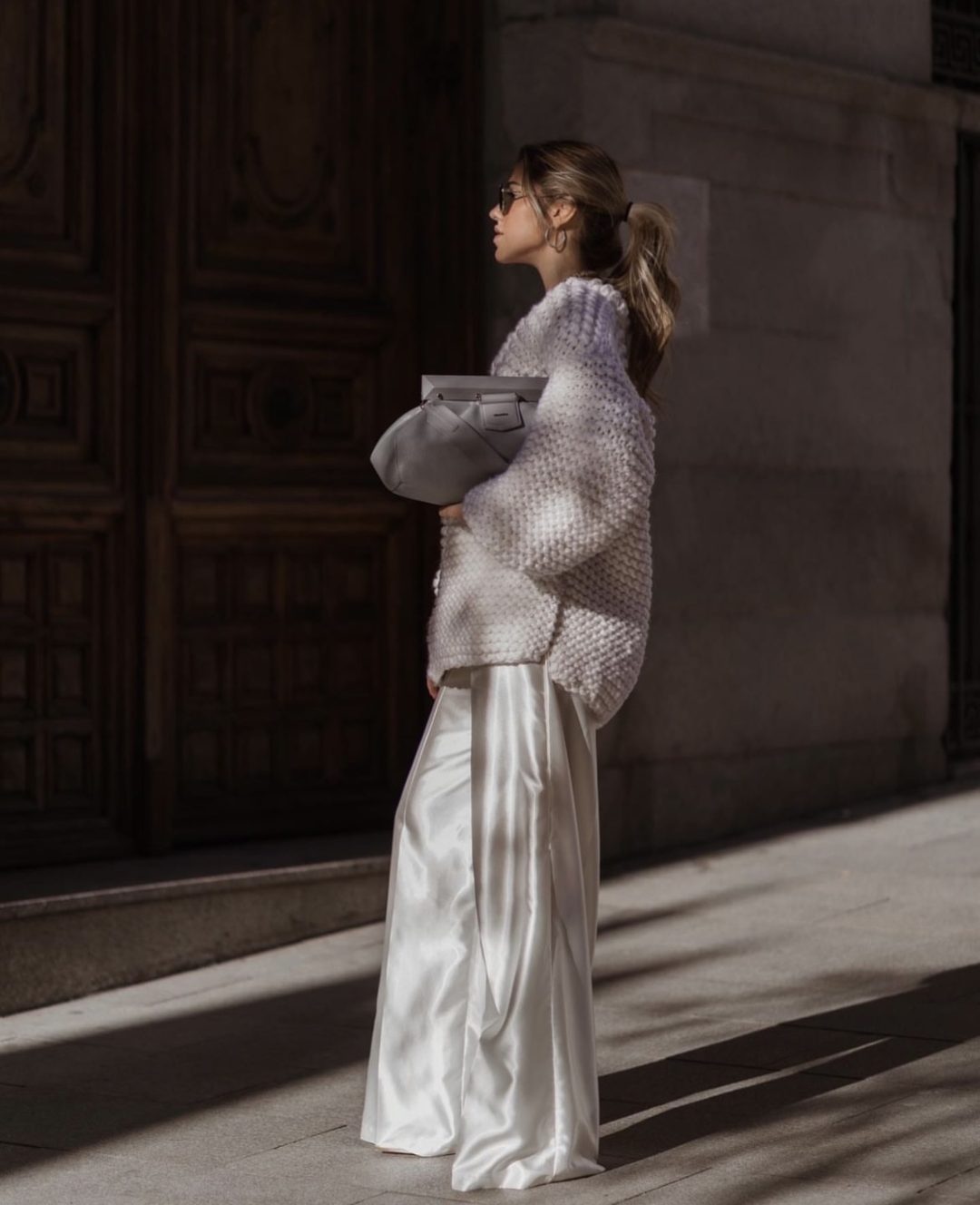 Girl wearing a chunky grey sweater with silver shiney palazzo pants and a grey clutch bag