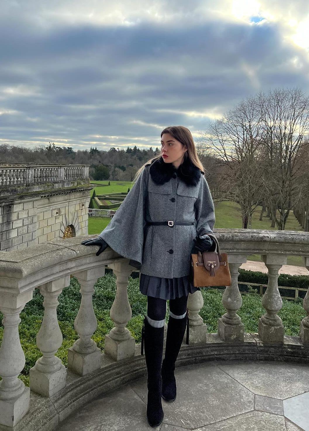 Preppy grey cape jacket outfit with black knee high boots and a pleated mini skirt.