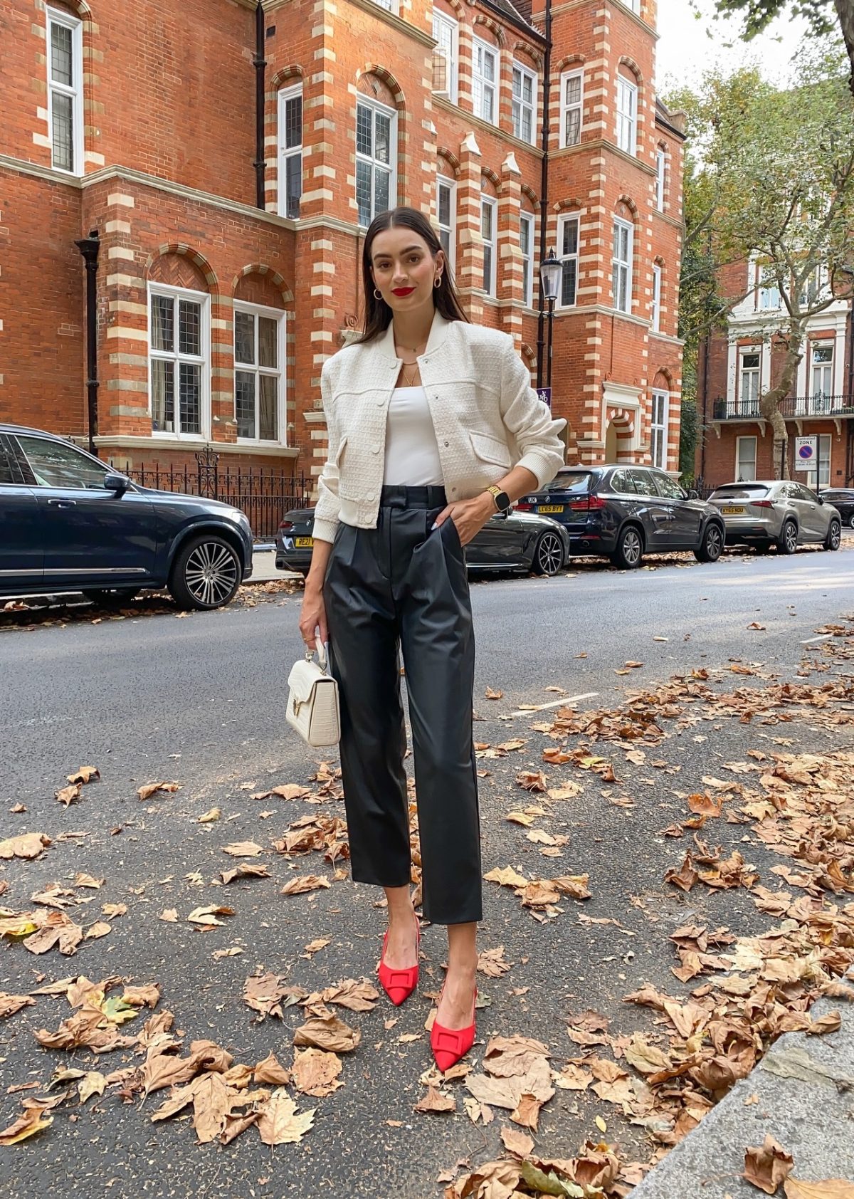 Chic outfit with black leather pants, white structured cardigan and red heels.