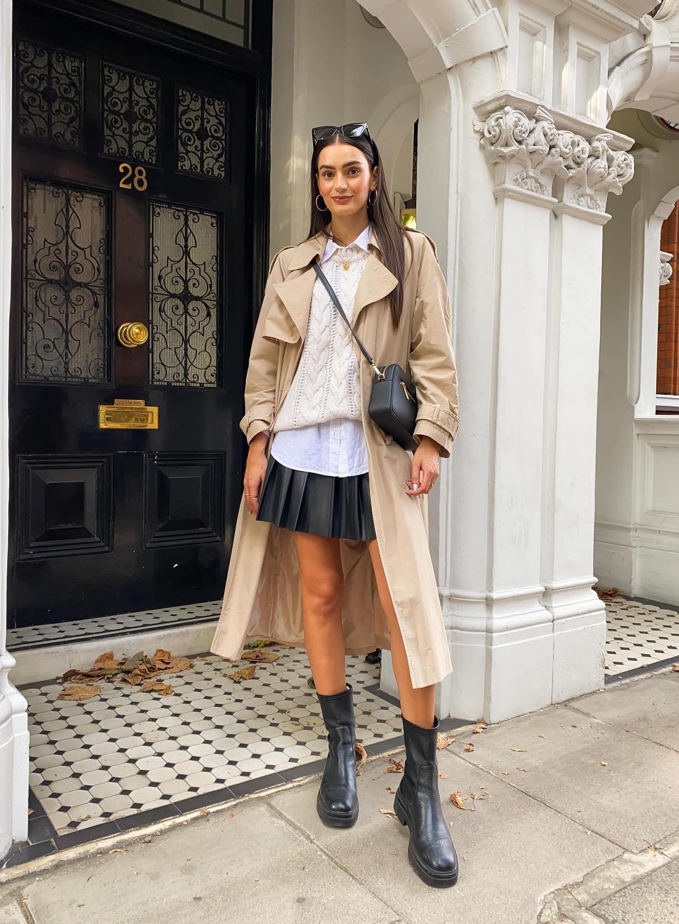 Preppy outfit with a black pleated mini skirt, a trench coat and black ankle boots.