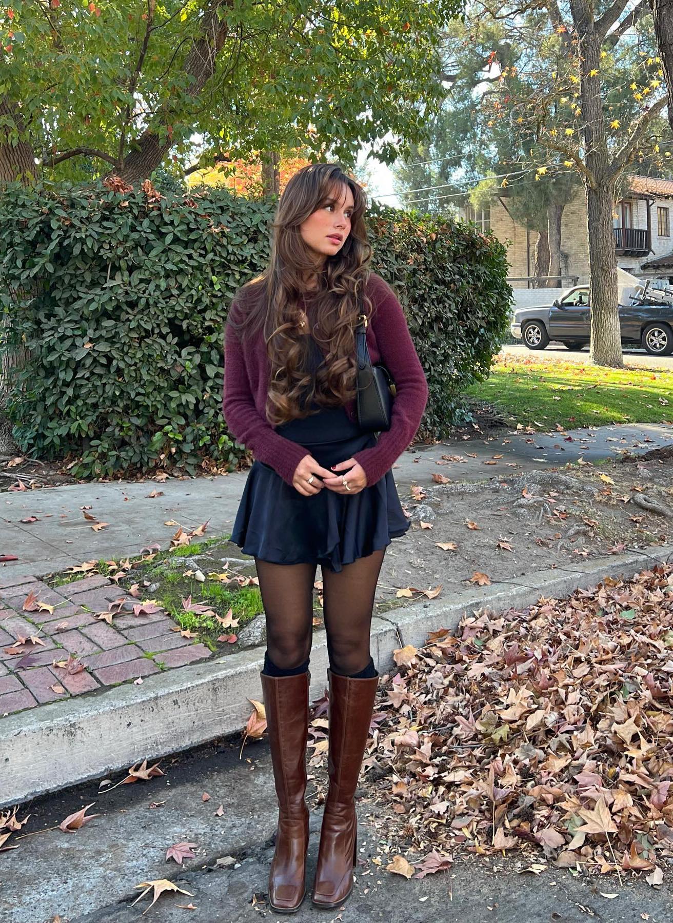 Preppy outfit with a short black mini skirt, brown knee-high boots and a burgundy cardigan.