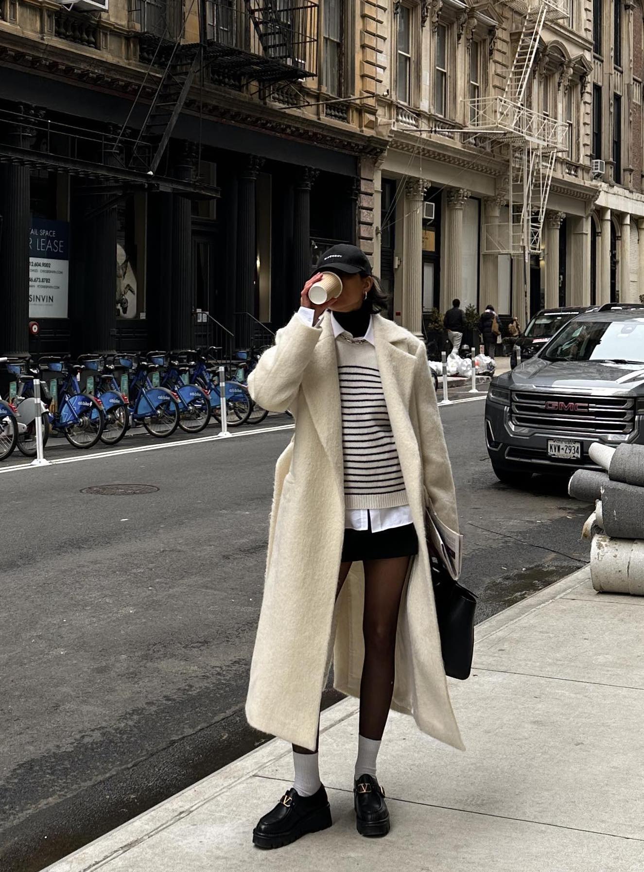 Cute winter outfit with a long white coat, black mini skirt and preppy loafers.