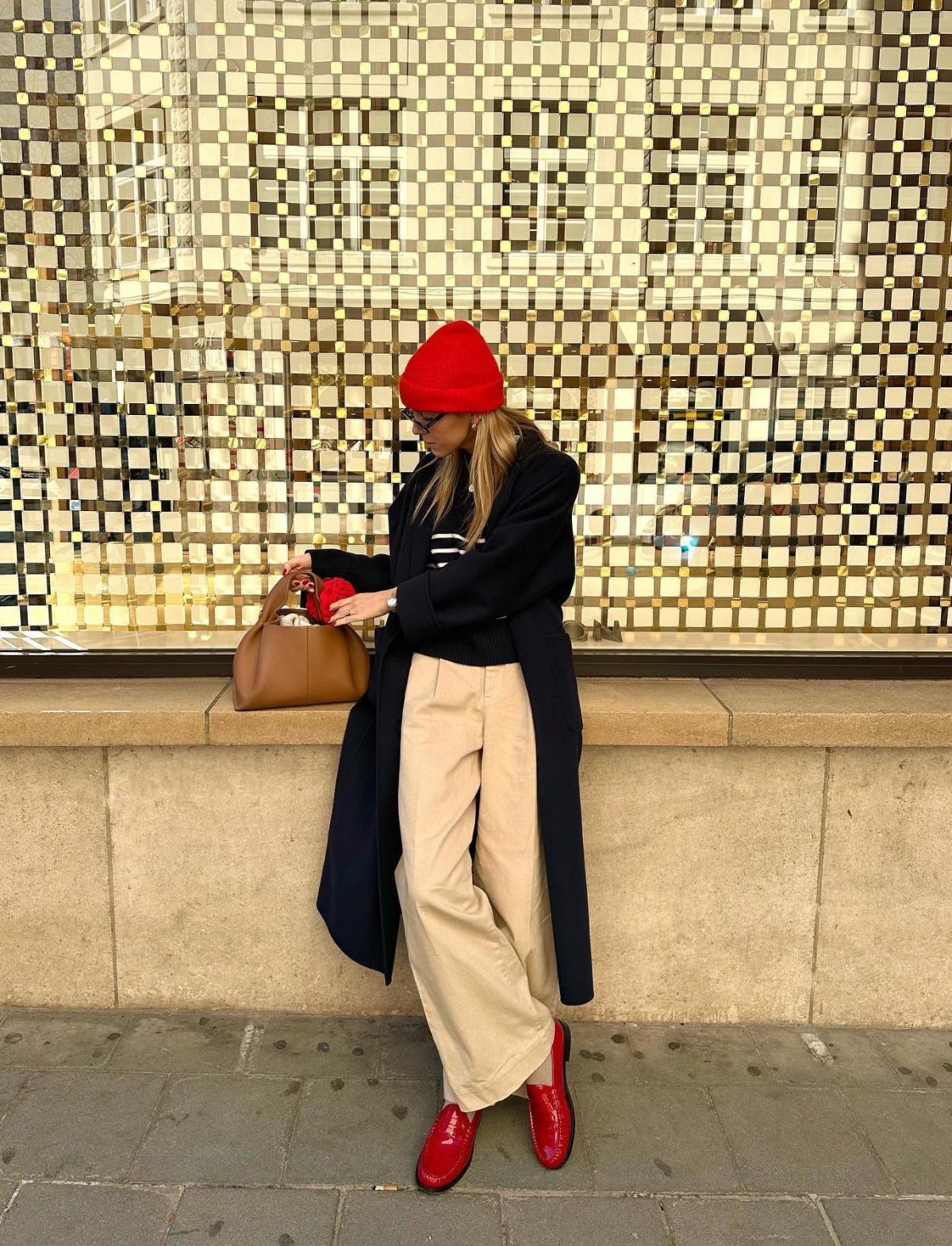 Casual outfit with a black trench coat, beige wide-leg pants, red loafer shoes and a red hat.