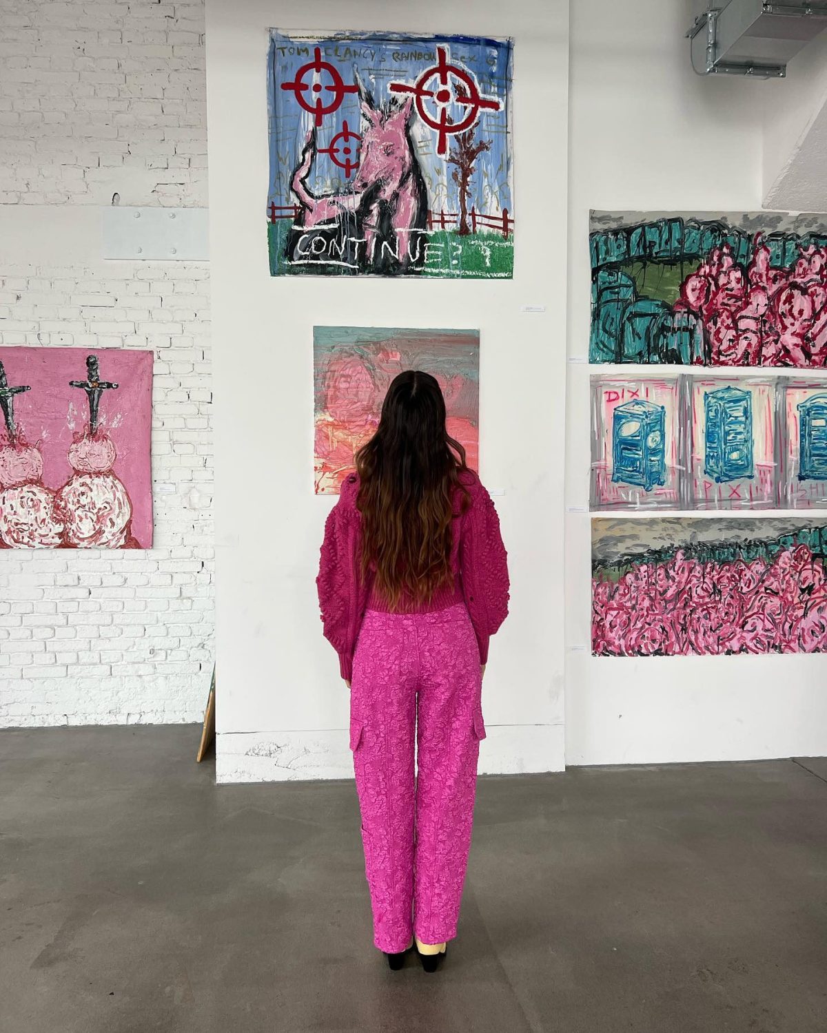 A woman standing in a museum with her back to the camera wearing a pink shirt and pink lacy cargo pants