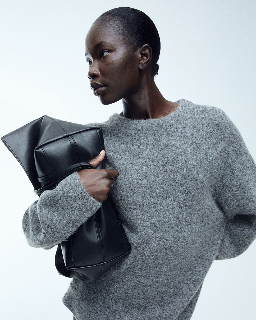 Close-up of a woman wearing a soft grey crewneck sweater and carrying a black leather tote bag