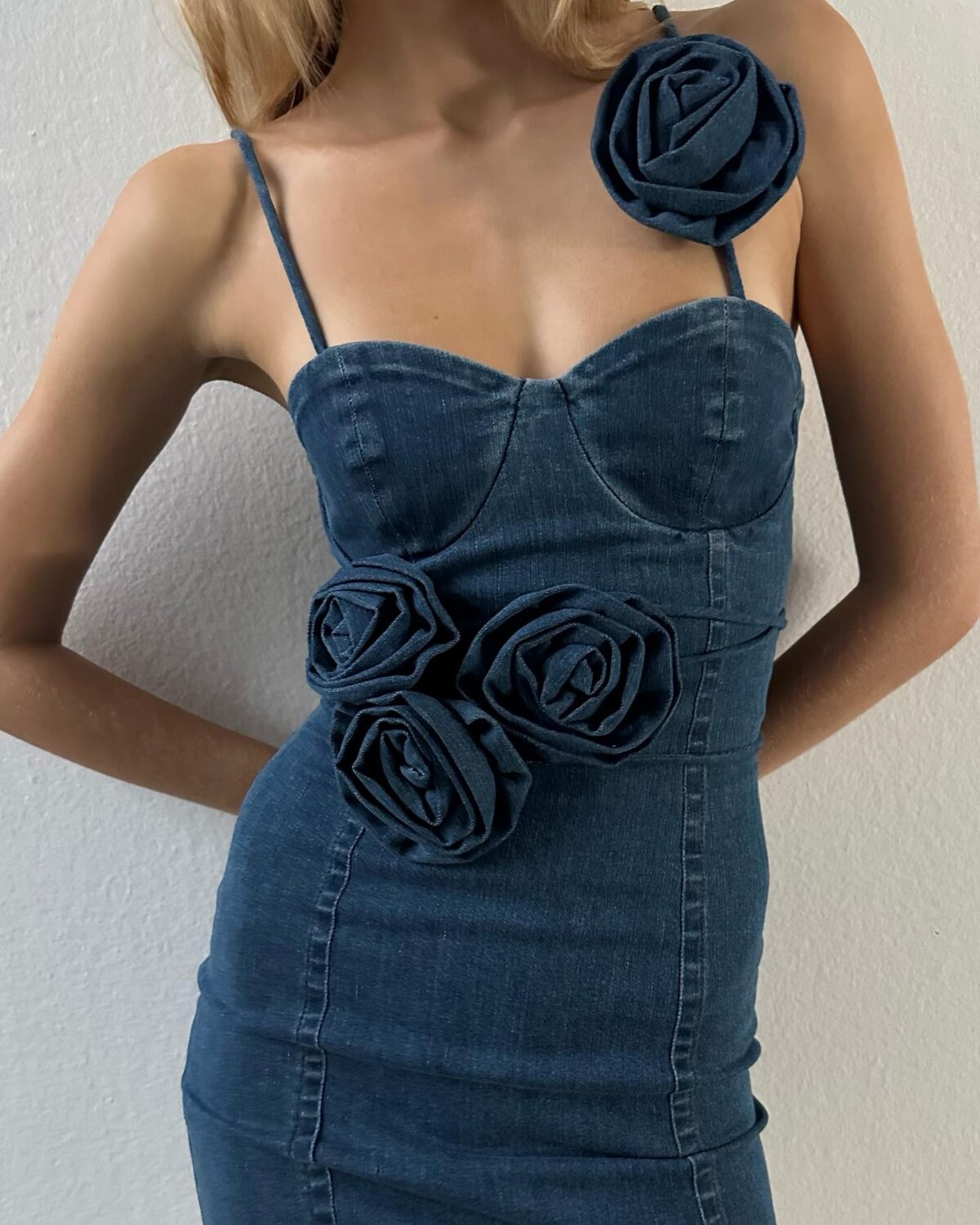 Woman from the neck down wearing a dark blue denim dress decorated with roses