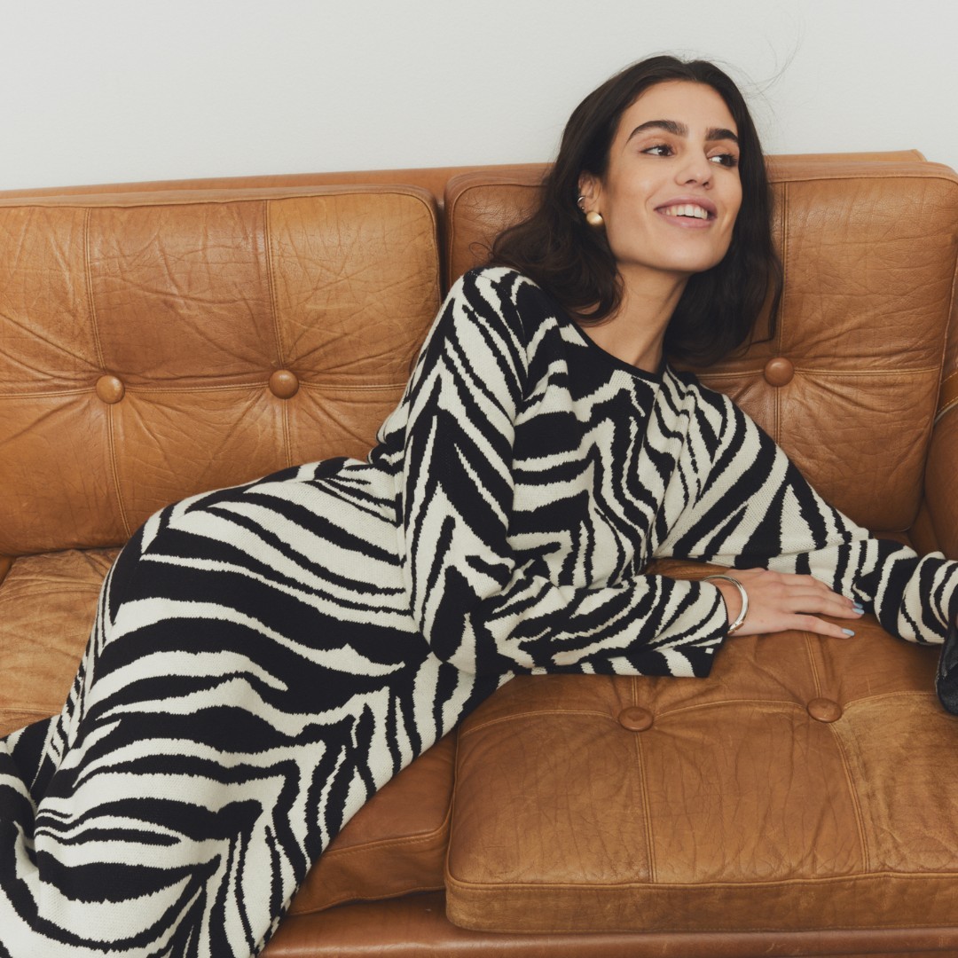 Dark haired woman lounging on a sofa wearing a black and white zebra patterned midi dress