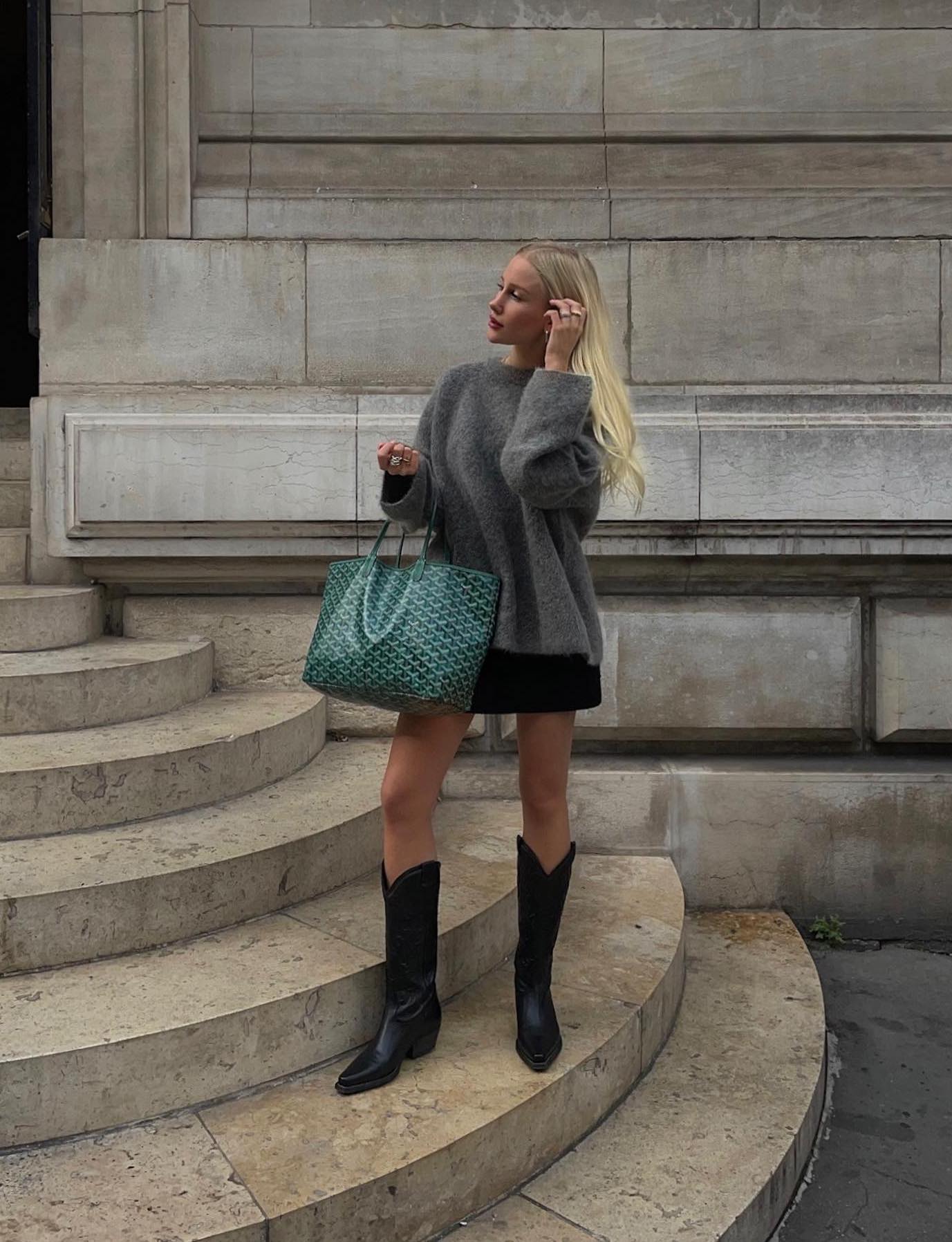 Casual outfit with a grey cashmere sweater, mini skirt, black cowboy boots and a green Goyard tote bag.