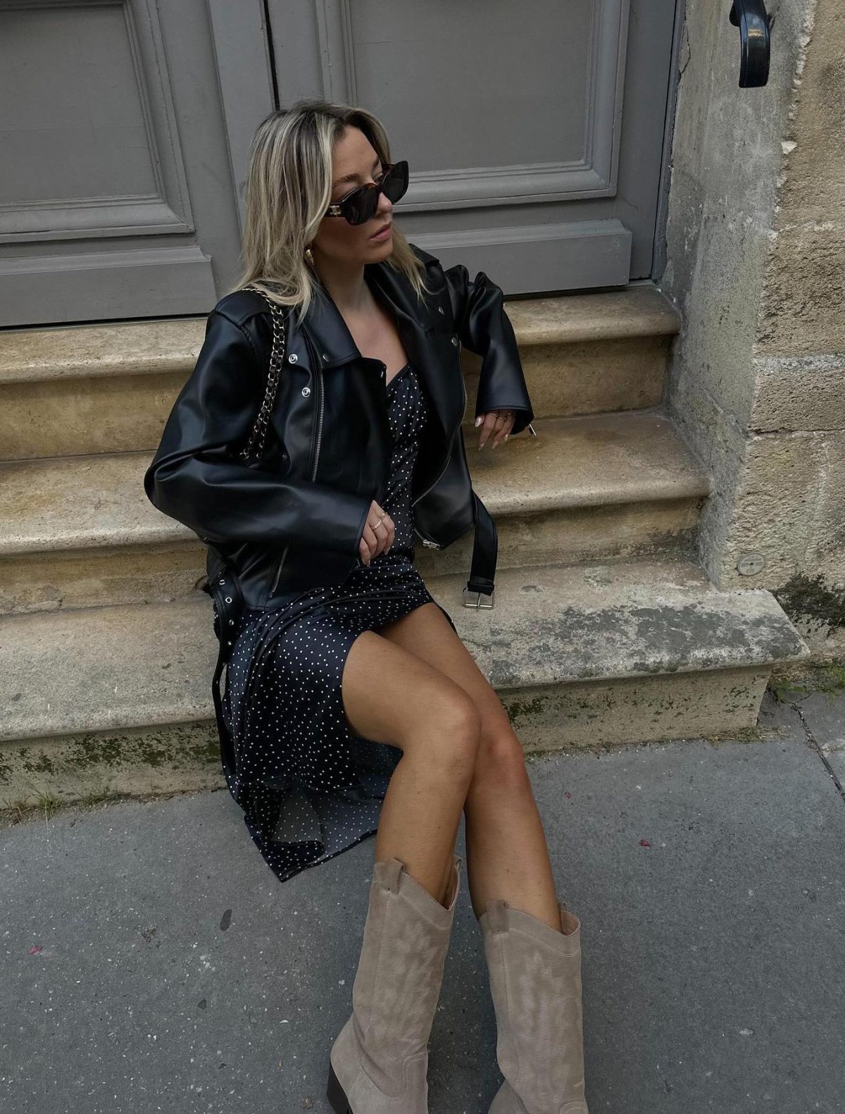 Cool spring outfit with a black leather jacket, polka dot midi dress and beige cowboy boots.