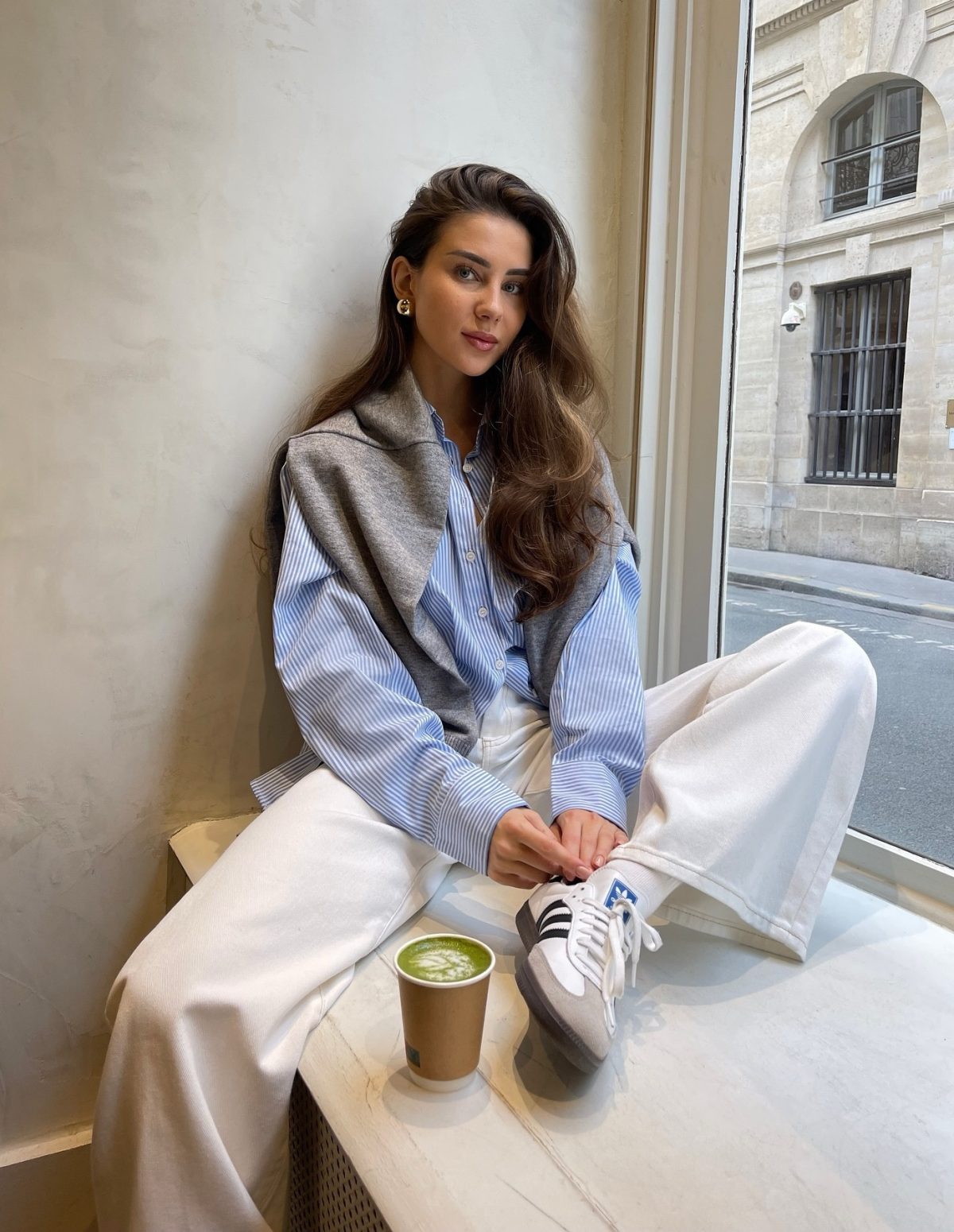 White jeans with Adidas Samba sneakers and a blue button-up shirt.