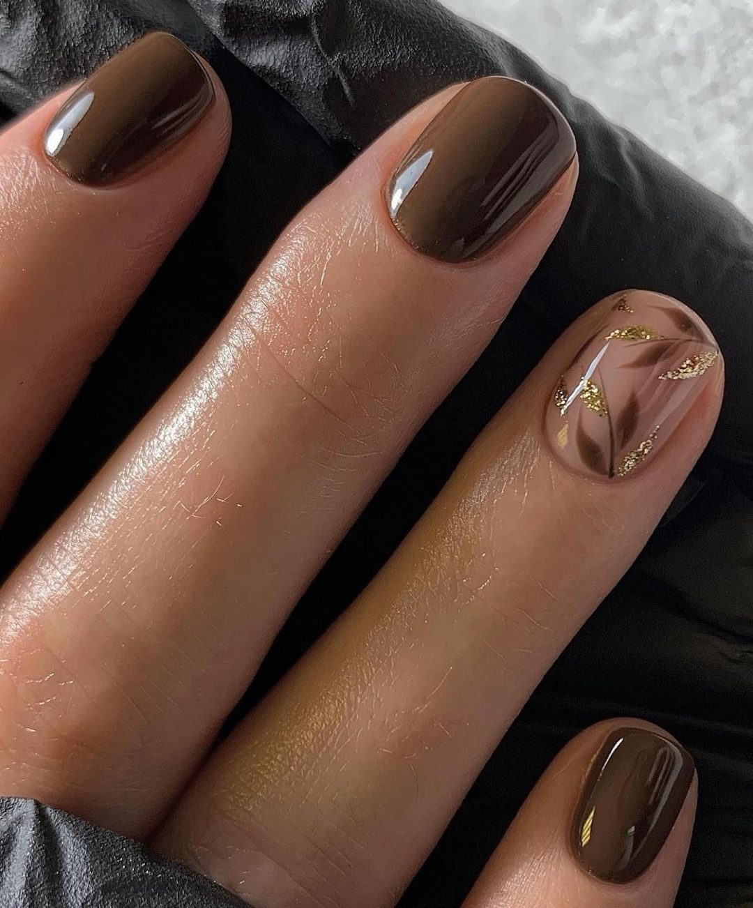 Unhas curtas marrons com nail art em folhas.