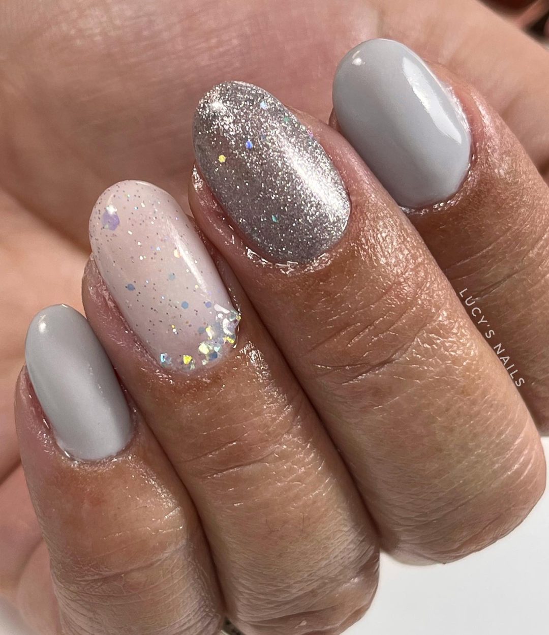 Unhas curtas cinza claro com glitter.