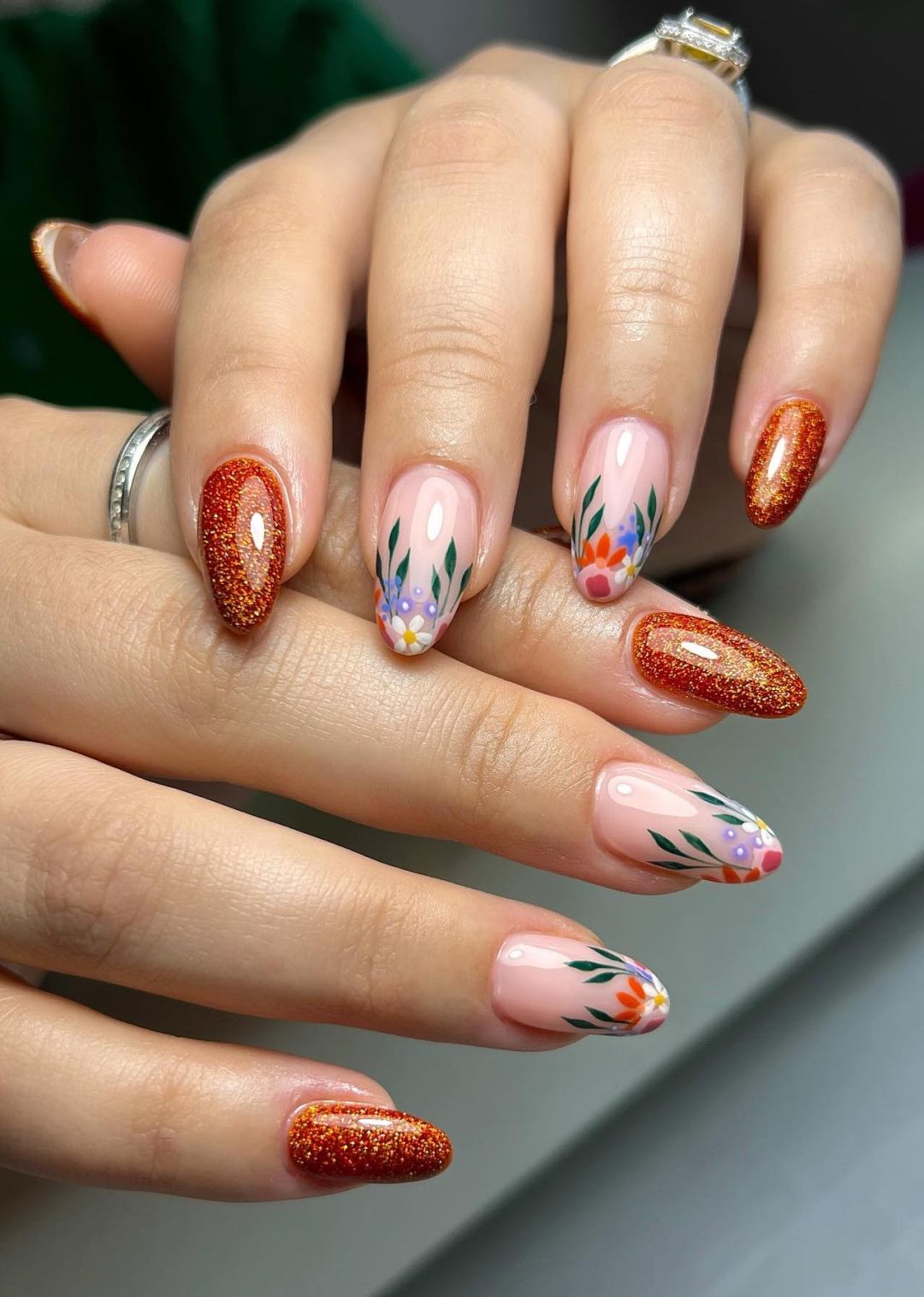 Uñas con brillo color naranja quemado y flores otoñales.