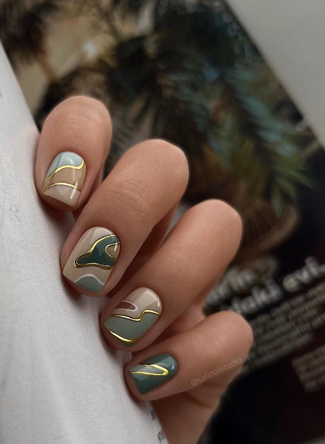 Short abstract green nails with gold swirls.