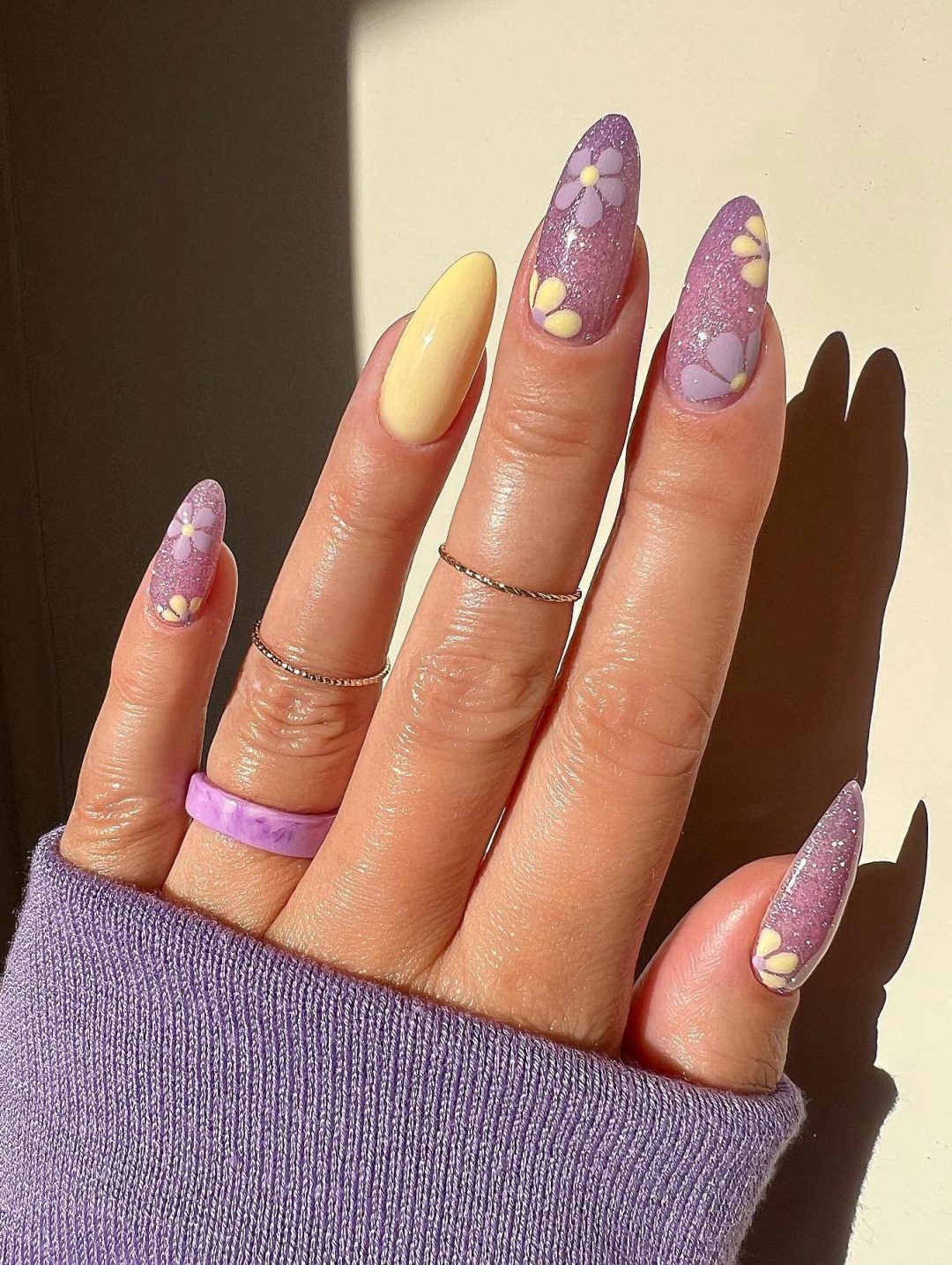 Pastel purple and pale yellow nails with glitter and flowers.