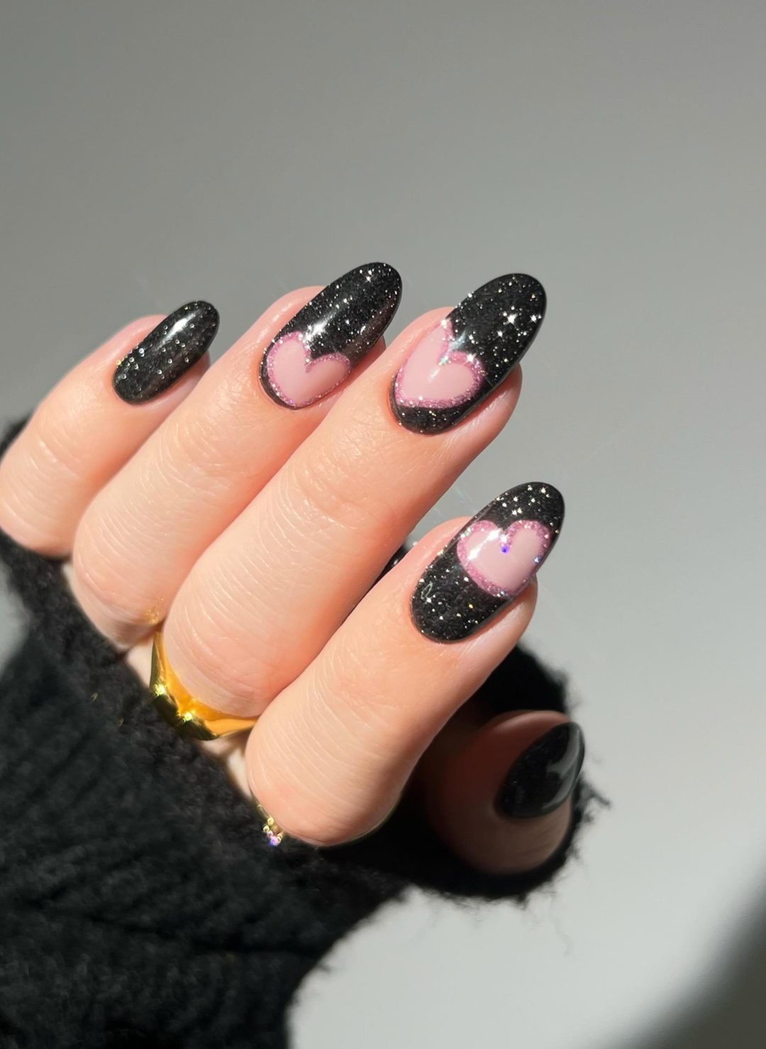 Black glitter nails with pink hearts.