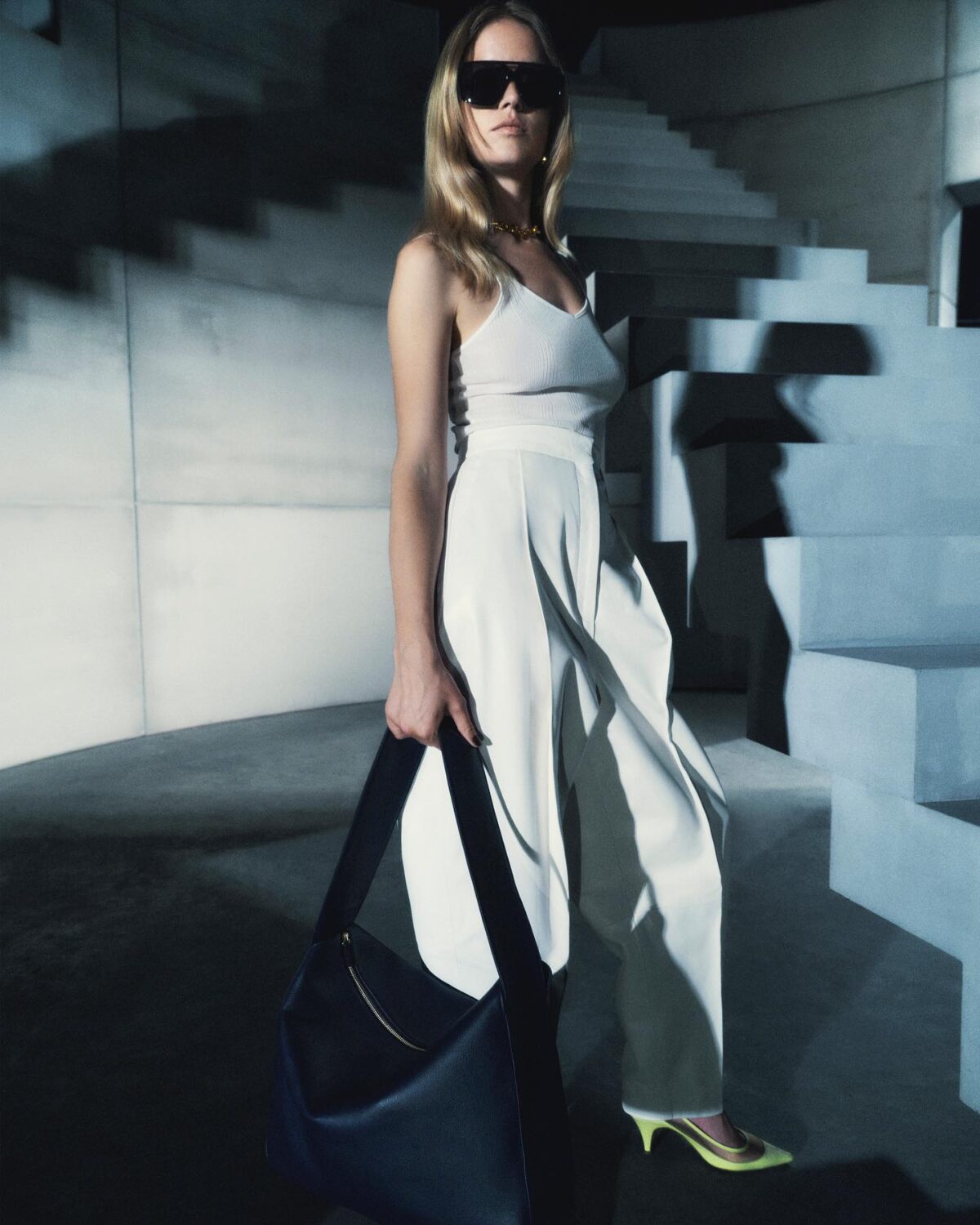 Smart outfit with a white tank top, white wide leg pants, a black handbag and green kitten heel shoes