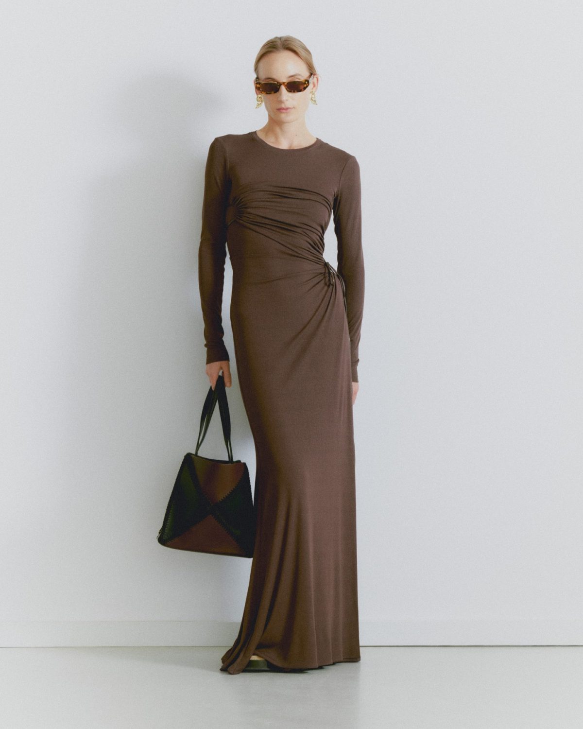 Blonde woman wearing a long sleev brown maxi dress with brown sunglasses and a black and brown handbag