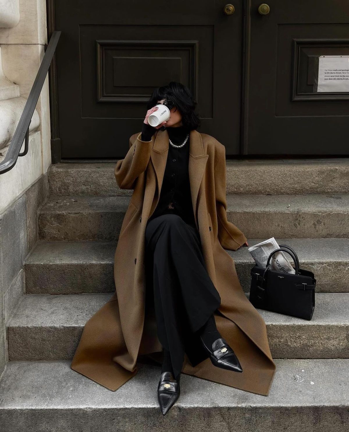 Chic outfit with black pants, a black sweater, black loafers and a long brown wool coat