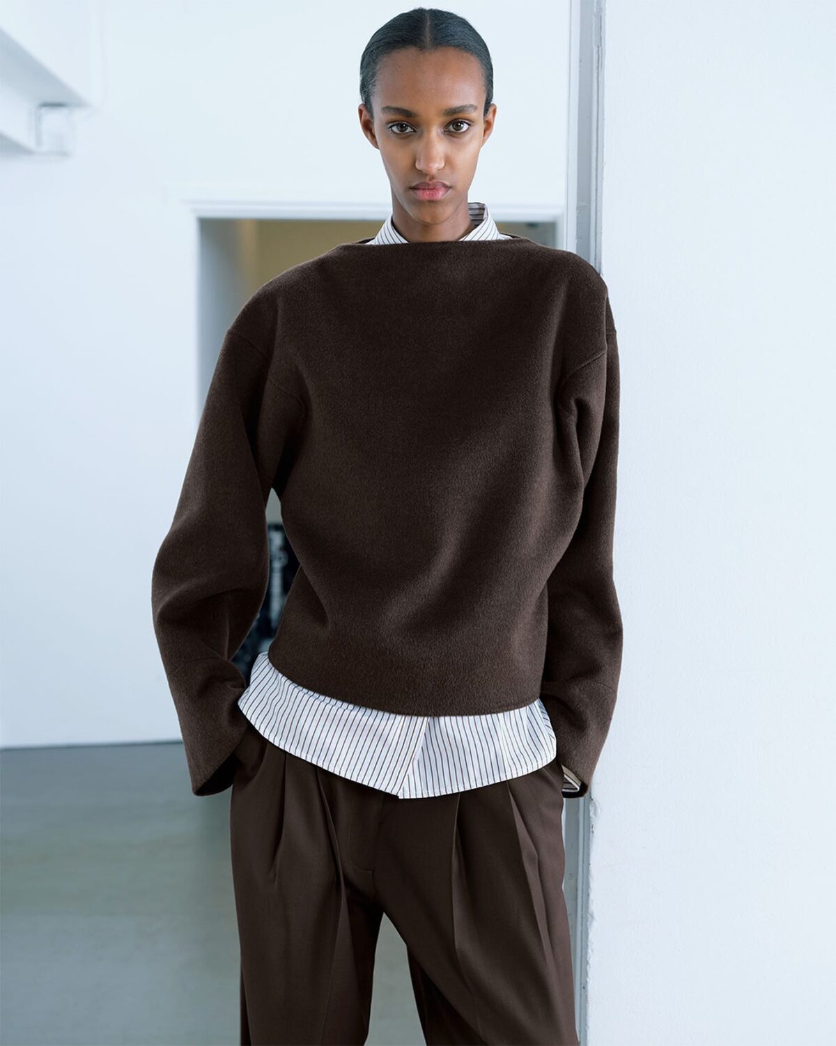 Smart outfit with a striped button-up shirt, a brown sweater over the top and brown pleated pants