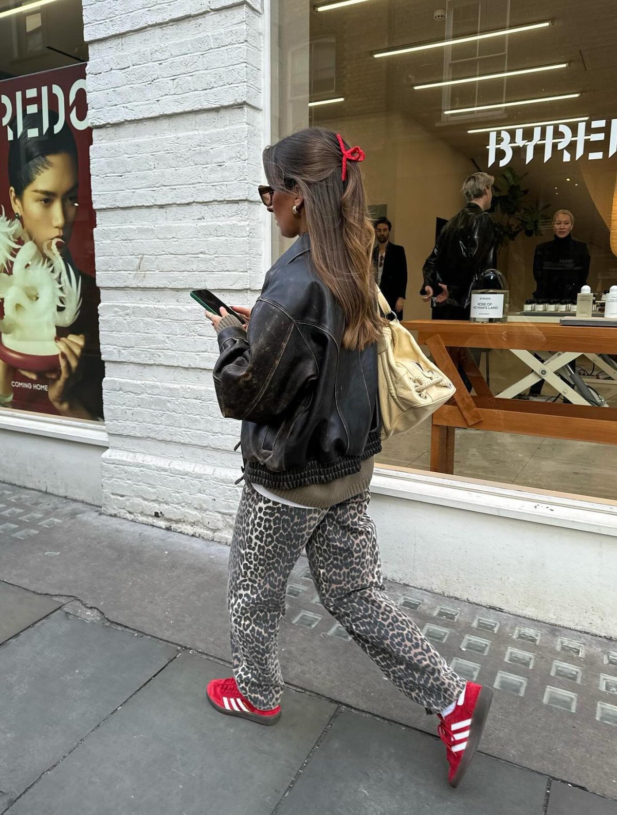 Casual leopard print pants with a brown leather jacket and red Adidas Gazelle sneakers