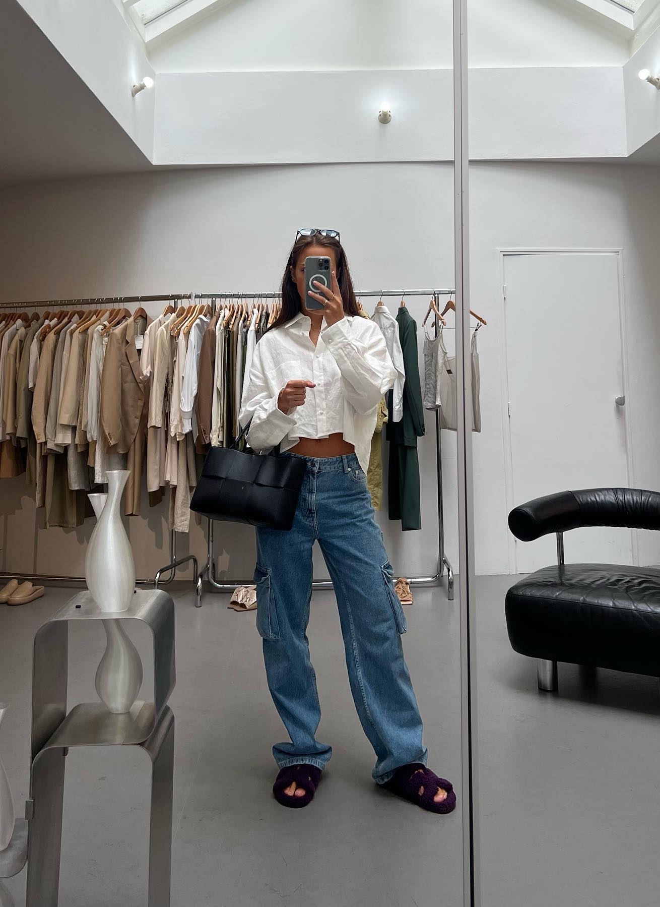 Casual outfit with low-rise jeans, a white button-up shirt, Hermes Chypre sandals and a black Bottega Veneta Arco tote bag.