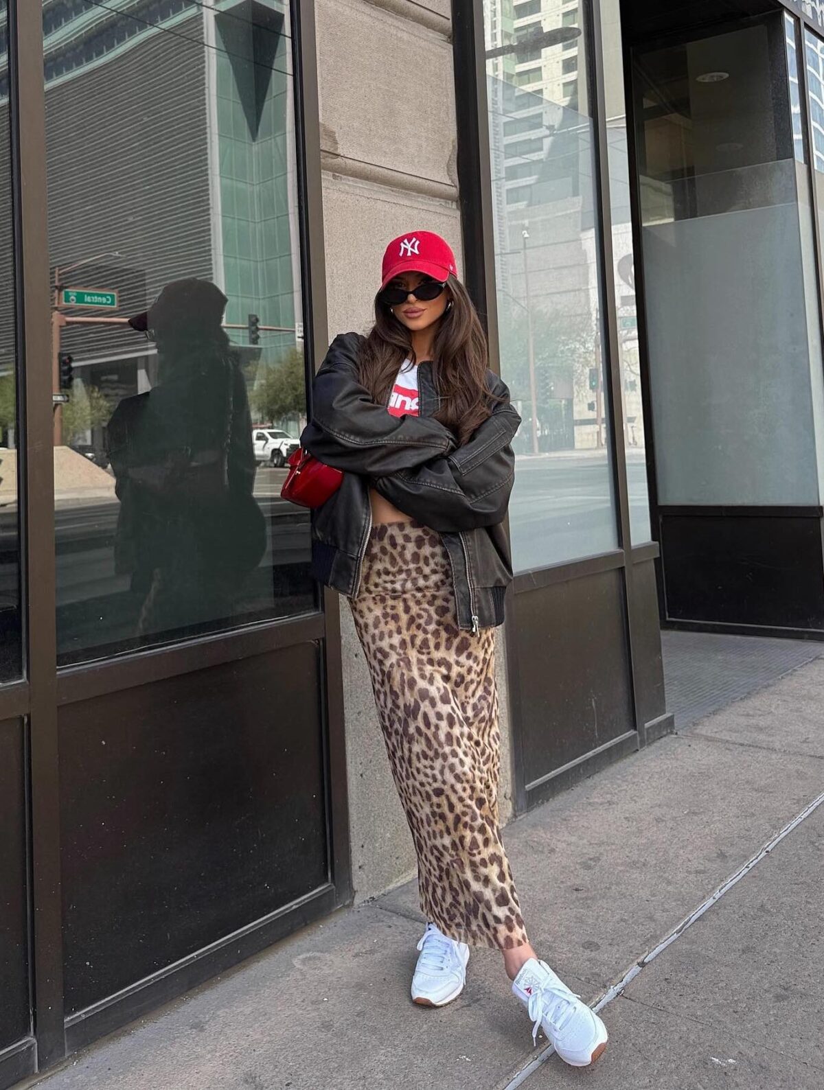 Long leopard print skirt with a dark brown leather jacket white sneakers and a red baseball cap